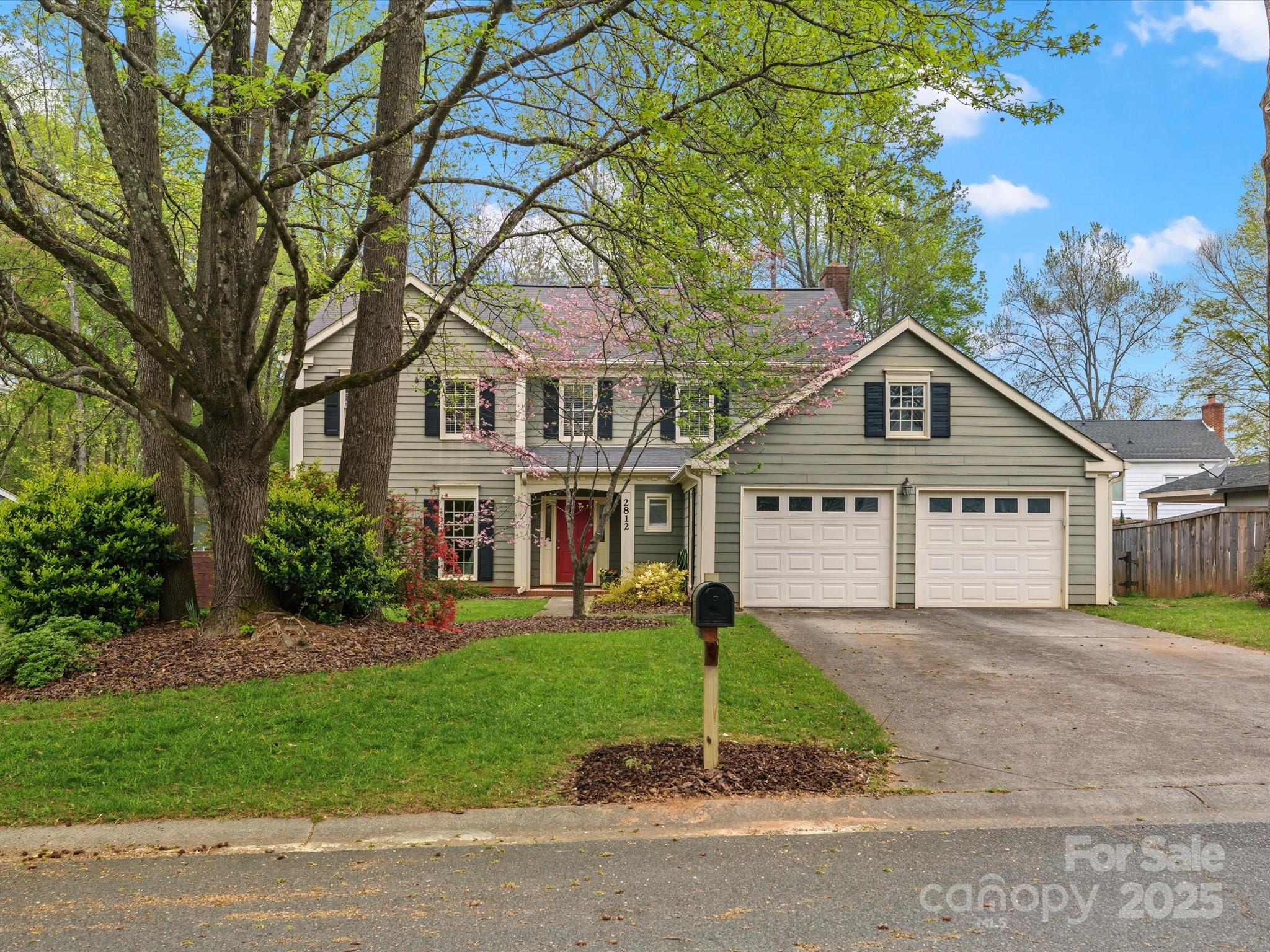 a view of a house next to a yard with plants and large trees
