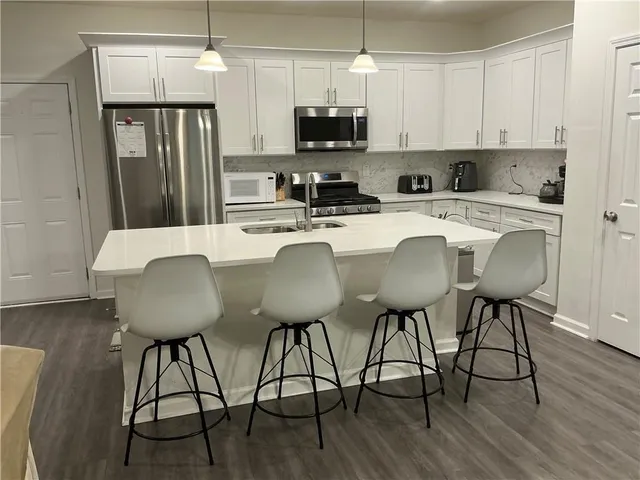 a kitchen with stainless steel appliances granite countertop a stove a refrigerator a kitchen island a dining table and chairs with wooden floor