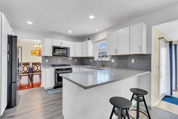 a kitchen with stainless steel appliances granite countertop a stove a sink a microwave a refrigerator white cabinets and wooden floor