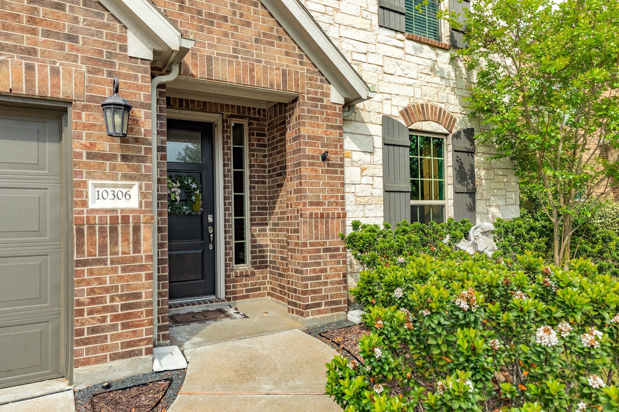 10306 Aldrin Drive Rosharon, TX 77583 - Photo 2 of 50 The property features an inviting exterior, highlighted by a beautiful stone facade, a stunning wooden front door, and well-manicured landscaping.