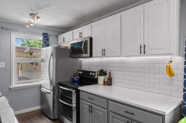 961 33rd Street Ogden, UT 84403 - Photo 13 of 39 Bright kitchen featuring two-tone cabinetry with modern hardware, stainless steel appliances, a subway tile backsplash, under-cabinet lighting, and light-toned countertops
