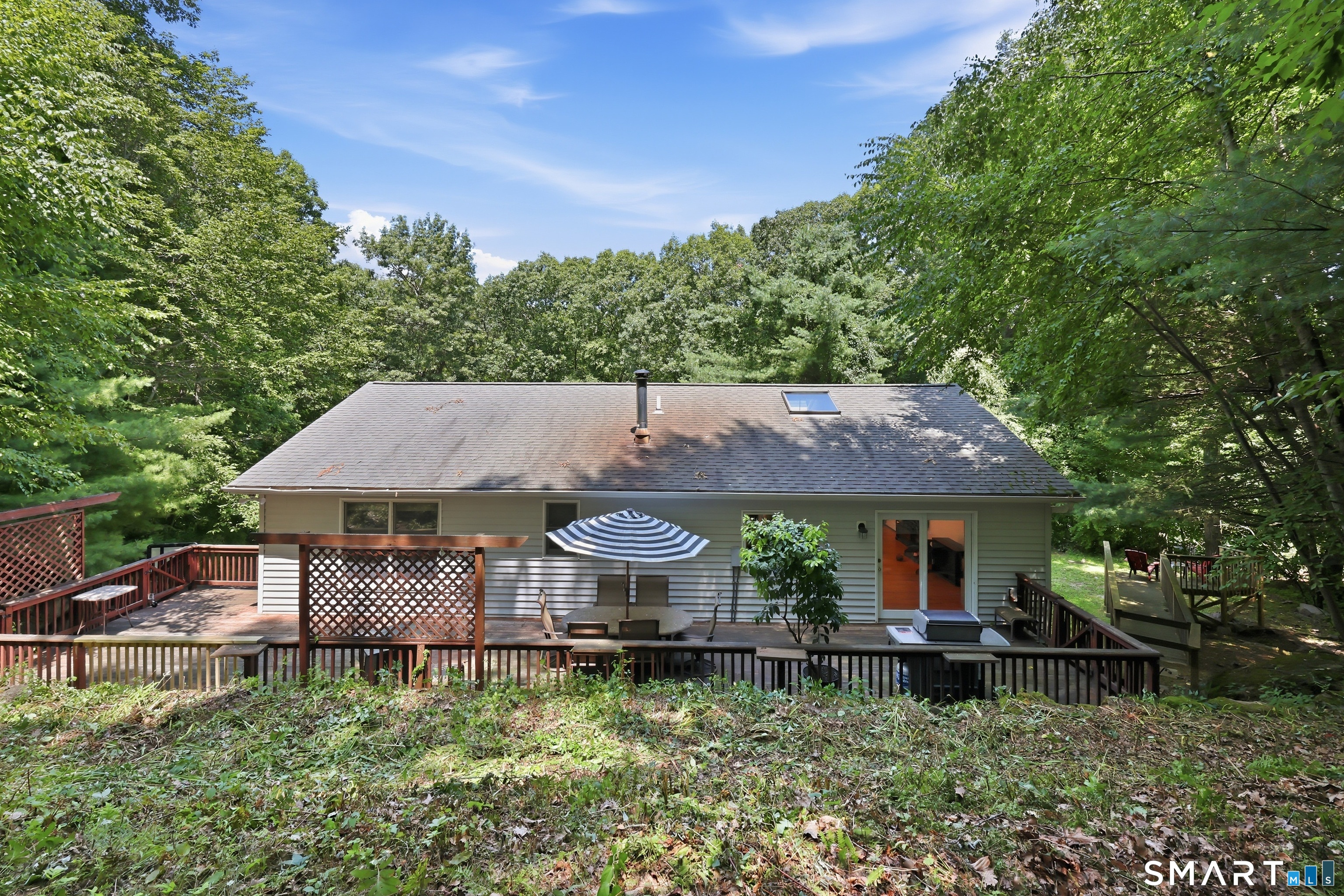8 Old Bridge Road West New Fairfield, CT 06812 - Photo 27 of 35 Expansive rear deck nestled beneath a mature tree canopy, offering a cool, shaded retreat for outdoor dining, entertaining, or simply relaxing all summer long.