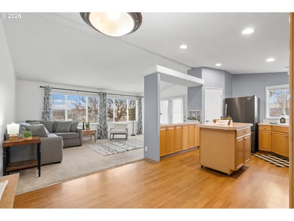 a living room with stainless steel appliances kitchen island granite countertop a refrigerator a stove a sink dishwasher and a dining table with wooden floor