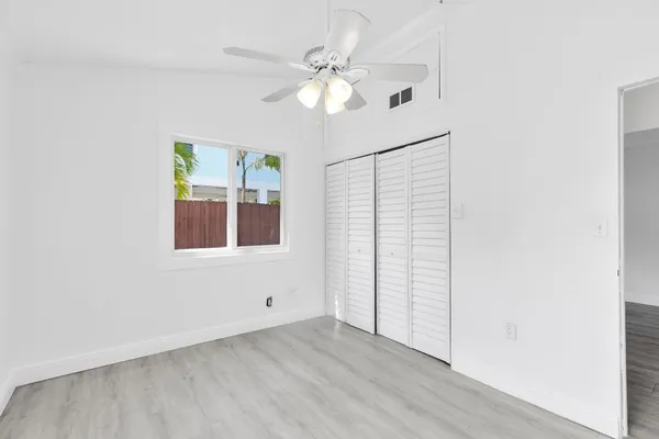 an empty room with wooden floor chandelier fan and windows