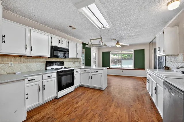 a large kitchen with a stove top oven a sink dishwasher white cabinets and wooden floor