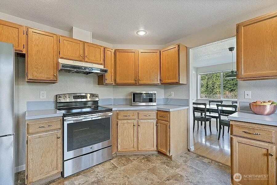 Undisclosed Address Redmond, WA 98052 - Photo 7 of 31 a kitchen with stainless steel appliances granite countertop a stove top oven a sink dishwasher a dining table and chairs with wooden cabinets