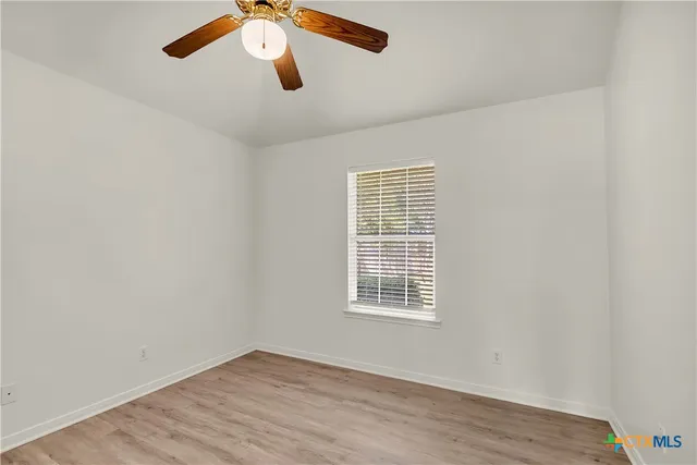 an empty room with a window a ceiling fan and wooden floor