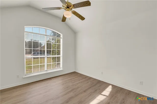 an empty room with wooden floor fan and windows