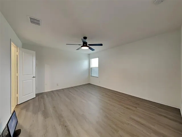an empty room with wooden floor chandelier fan and windows