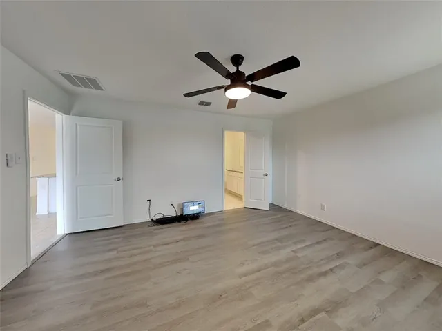a view of an empty room with wooden floor and a ceiling fan