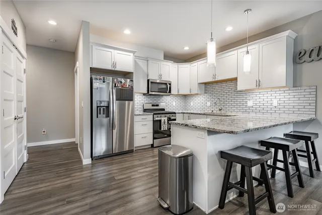 a kitchen with stainless steel appliances granite countertop white cabinets a sink a stove a refrigerator and island