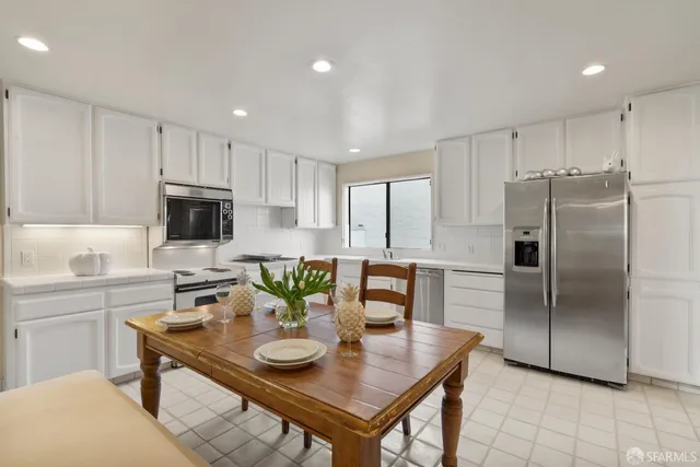 a kitchen with stainless steel appliances granite countertop a refrigerator a sink a stove a dining table and chairs