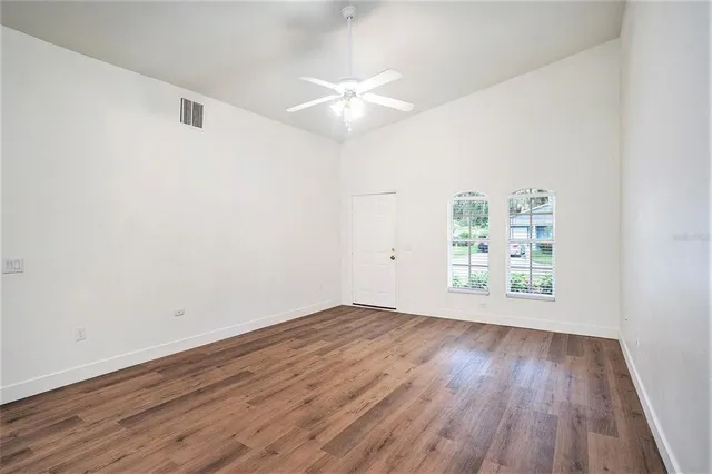 an empty room with wooden floor chandelier fan and windows
