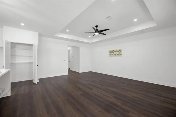a view of an empty room with wooden floor and a ceiling fan
