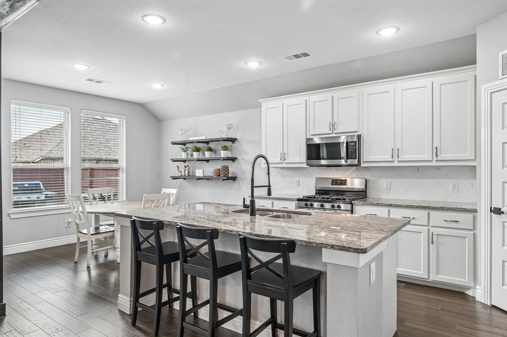 1805 Huntsman Way Forney, TX 75126 - Photo 13 of 34 Modern kitchen featuring a large island with a stone countertop, white shaker-style cabinetry, stainless steel appliances, dark wood-finish flooring, and recessed lighting