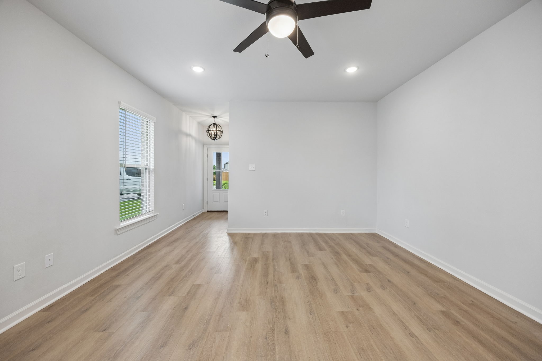 10902 Bonfire Trail Beasley, TX 77417 - Photo 6 of 36 This photo showcases a bright, open living space with light vinyl plank flooring, neutral walls, and recessed lighting. A ceiling fan is centrally located, and a window provides natural light. The area leads to an entryway with a decorative light fixture and a door to the outside.