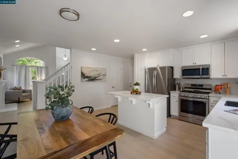 a kitchen with stainless steel appliances a white refrigerator a stove a microwave oven a sink with white cabinets and wooden floor