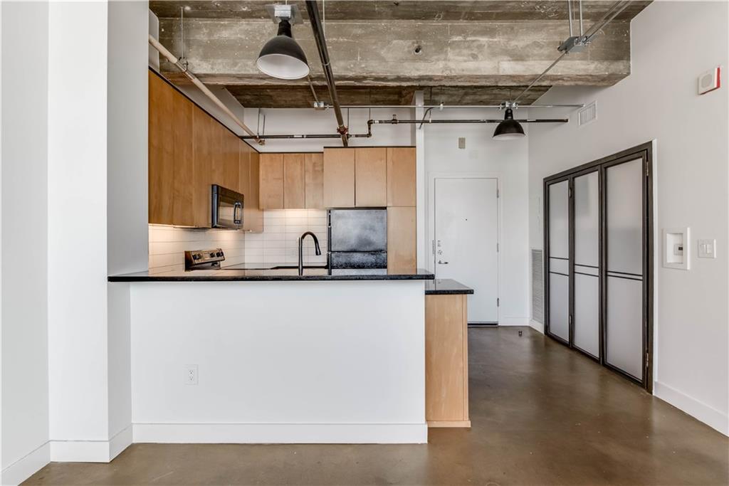 710 Colorado Street, Unit G9 Austin, TX 78701 - Photo 11 of 25 A modern kitchen island with granite countertops complements the exposed concrete ceiling and industrial-chic lighting.