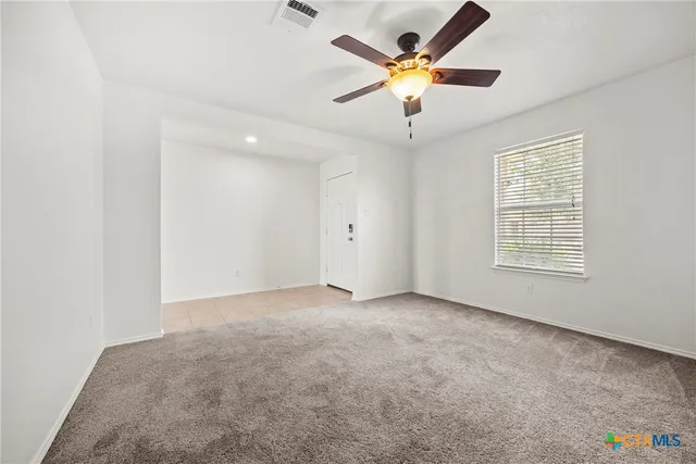 an empty room with chandelier fan and windows