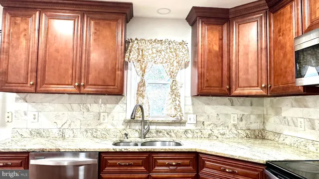 a kitchen with stainless steel appliances granite countertop wooden cabinets a stove top oven a granite counter tops and a view of living room