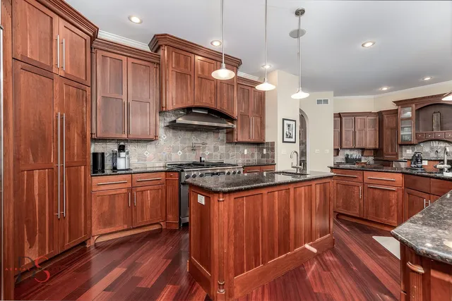 a kitchen with stainless steel appliances granite countertop wooden cabinets a sink a stove a refrigerator and island with wooden floor