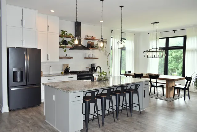 a kitchen with stainless steel appliances granite countertop a dining table chairs refrigerator a sink and a stove