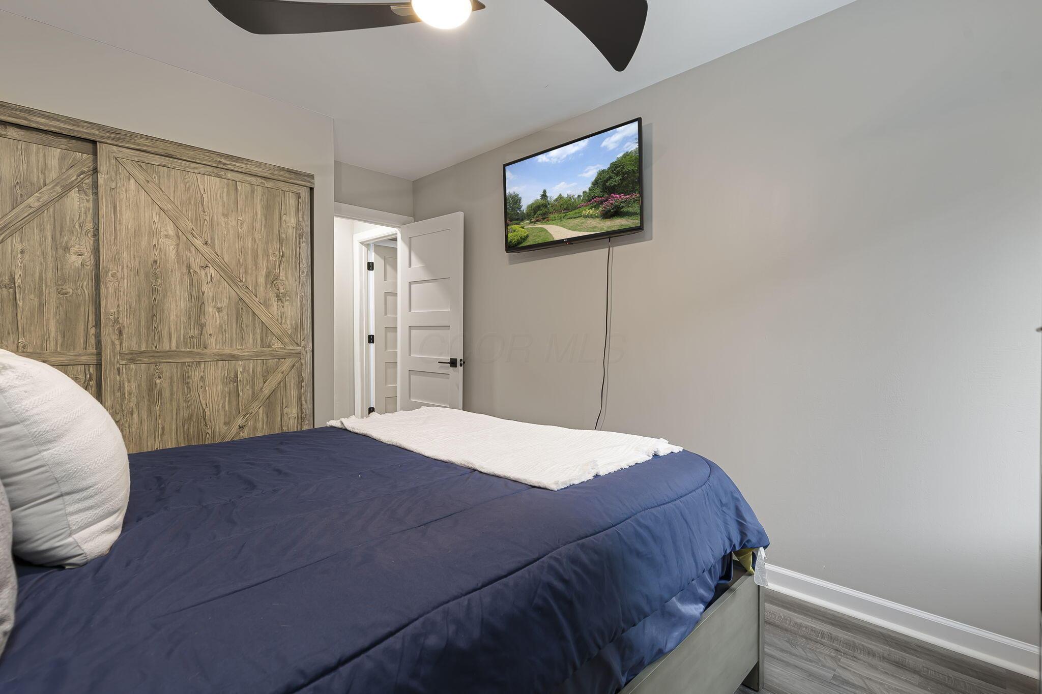 7140 Cook Road Powell, OH 43065 - Photo 58 of 87 Comfortable bedroom featuring a wood-finish barn door closet, ceiling fan with integrated lighting, wall-mounted flat-screen television, and neutral décor with coordinating bedding and pillows