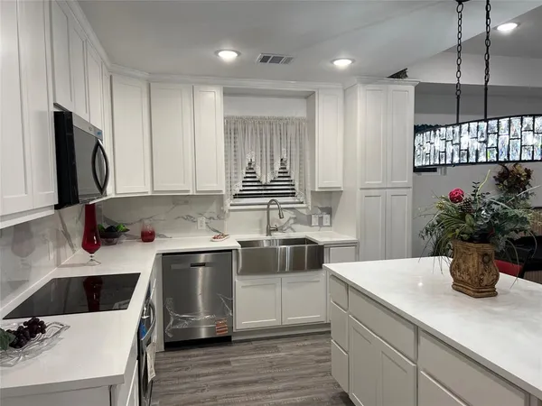 a large white kitchen with wooden floor and stainless steel appliances