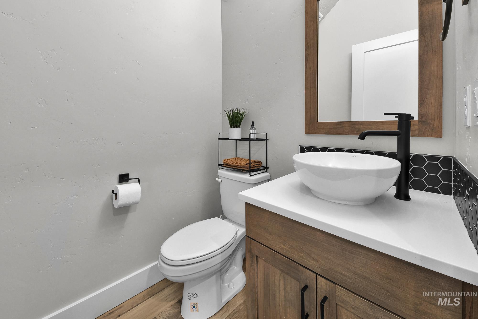 5676 East Zaffre Ridge Street Boise, ID 83716 - Photo 7 of 50 Powder room featuring a wood-finish vanity with a white countertop and vessel sink, matte black faucet, and a hexagonal tile backsplash