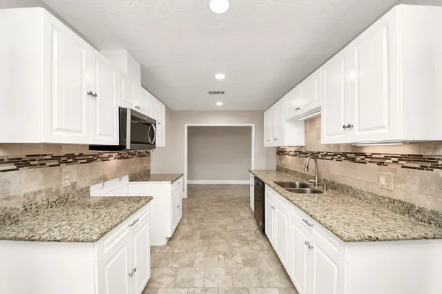 a large kitchen with granite countertop a sink and white cabinets