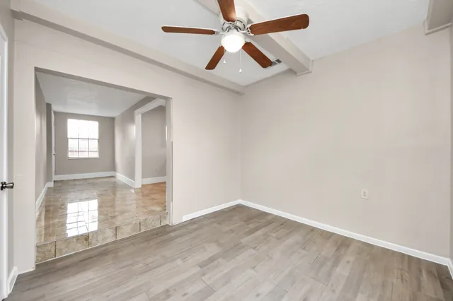 an empty room with wooden floor fan and windows