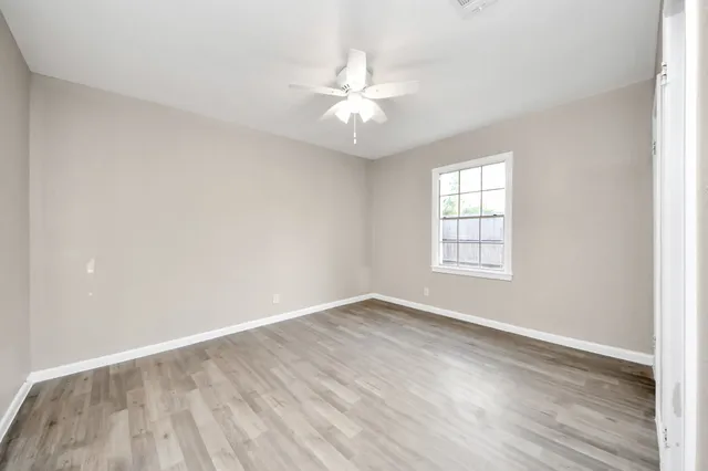 an empty room with wooden floor fan and windows