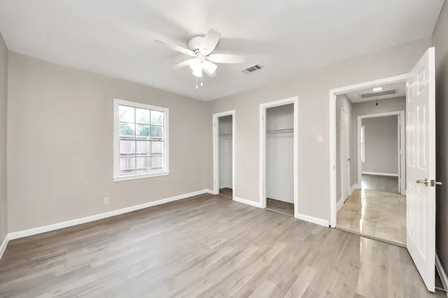 an empty room with wooden floor closet and windows