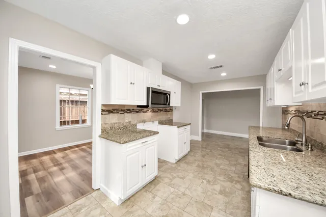 a large kitchen with kitchen island granite countertop a sink and white cabinets