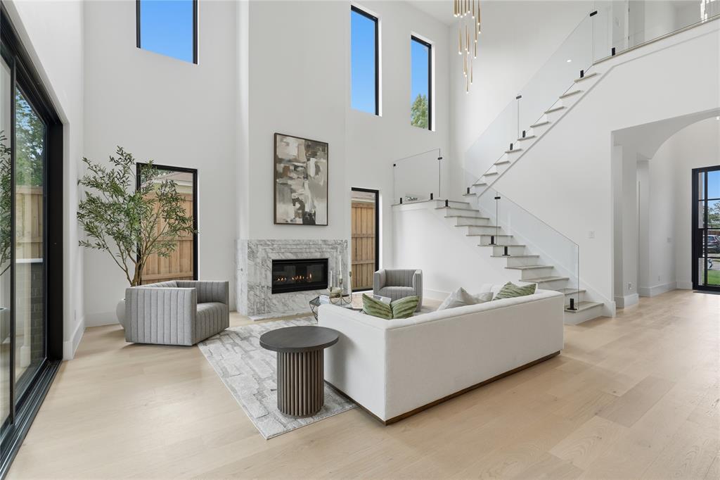 6038 Prospect Avenue Dallas, TX 75206 - Photo 16 of 40 Two-story living area featuring a marble-clad fireplace, light wood-finish flooring, and a contemporary open-riser staircase with glass railing