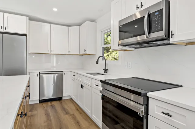 a kitchen with white cabinets appliances and a window