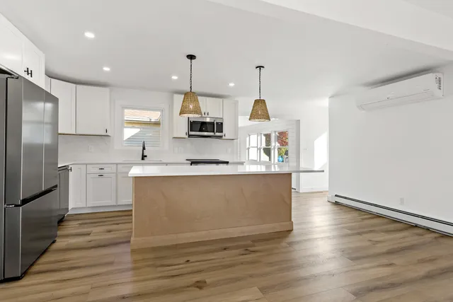 a view of a kitchen with kitchen island a sink wooden floor and stainless steel appliances