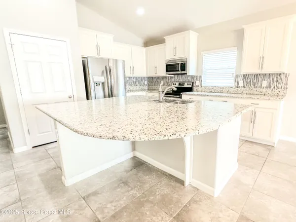 a kitchen with stainless steel appliances granite countertop a sink a stove a microwave a refrigerator and white cabinets