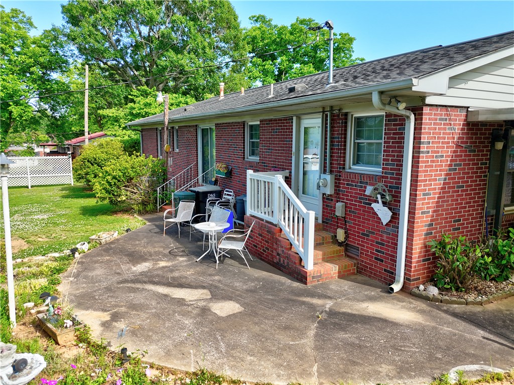 307 Calhoun Road Belton, SC 29627 - Photo 8 of 30 A spacious concrete patio awaits outdoor entertaining, nestled beside a charming brick facade with mature greenery.