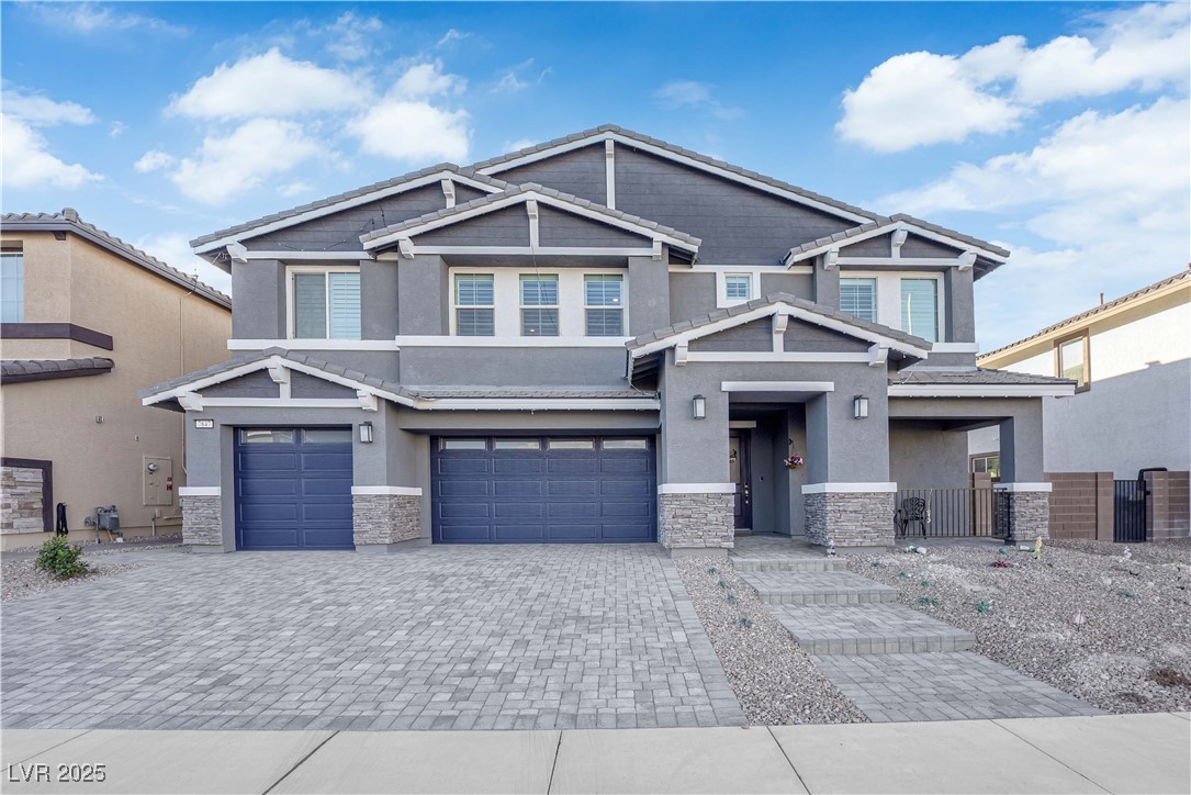 Craftsman-style home featuring stone siding, stucco siding, decorative driveway, and an attached garage