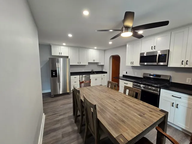 a kitchen with stainless steel appliances granite countertop a stove a refrigerator a kitchen island a sink dishwasher a dining table and chairs with wooden floor