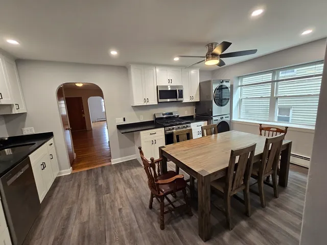 a kitchen with stainless steel appliances granite countertop a stove top oven a sink a refrigerator with a dining table and chairs with wooden floor
