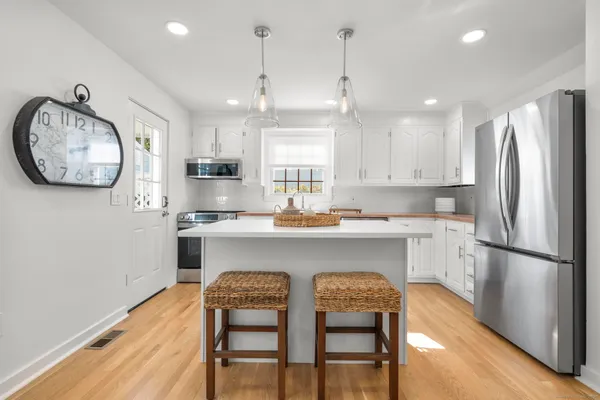 a kitchen with stainless steel appliances granite countertop a refrigerator a sink a stove a dining table and chairs with wooden floor