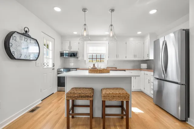 a kitchen with stainless steel appliances granite countertop a refrigerator a sink a stove a dining table and chairs with wooden floor