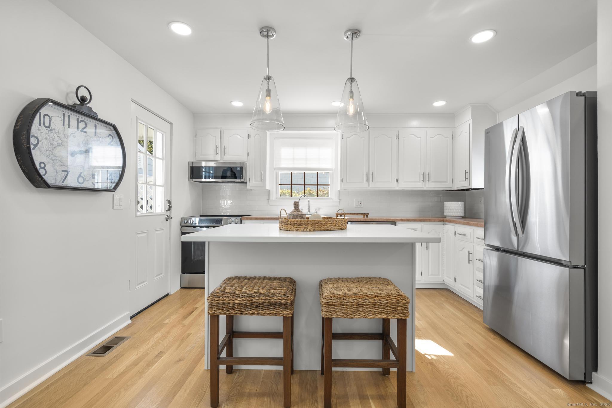 27 Reef Court Fairfield, CT 06824 - Photo 9 of 23 a kitchen with stainless steel appliances granite countertop a refrigerator a sink a stove a dining table and chairs with wooden floor