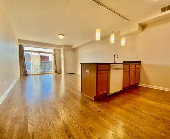 a view of a refrigerator in kitchen and an empty room with wooden floor
