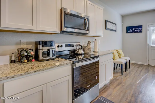 a kitchen with stainless steel appliances granite countertop a stove top oven a sink a dining table and chairs with wooden floor