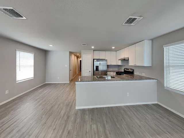 a kitchen with stainless steel appliances granite countertop a refrigerator a sink dishwasher a stove and white countertops with wooden floor