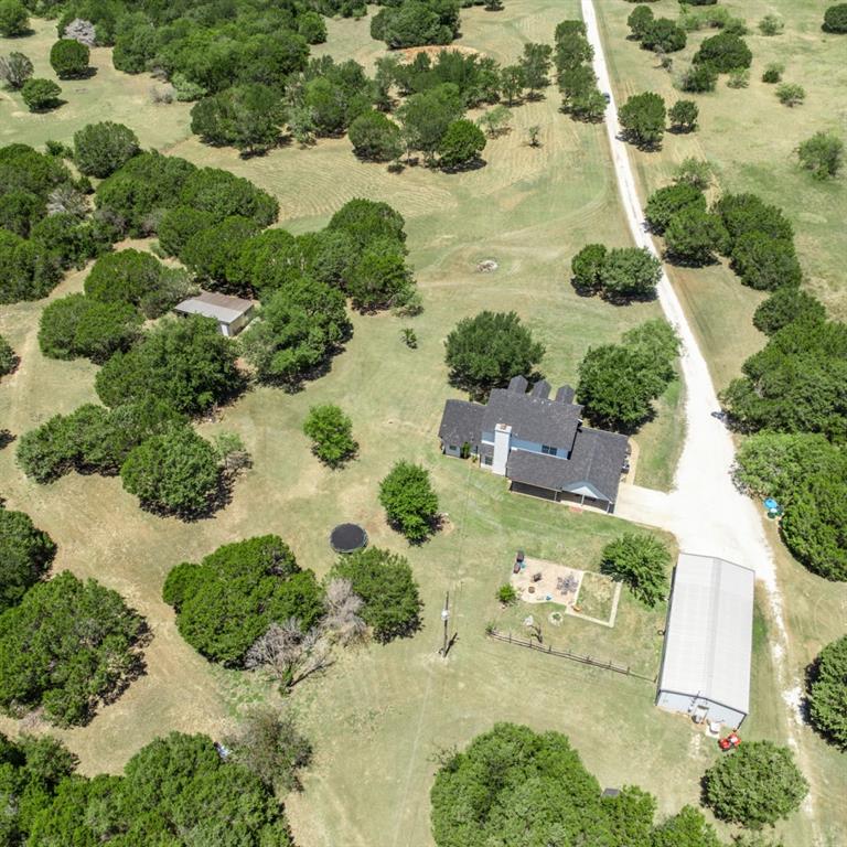 785 Tweedy Road Valley Mills, TX 76689 - Photo 37 of 40 Aerial perspective showcasing a sprawling property featuring a two-story residence, extensive green space, a metal outbuilding, and a gravel driveway