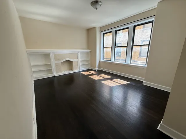 an empty room with wooden floor fireplace and windows